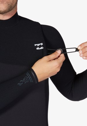 Traje de neopreno negro con tejido texturizado, que presenta un logotipo y un cordón ajustable. Manos demuestran el uso del cordón en el lateral del traje.