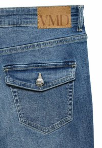 Spijkerbroeken in een lichtblauwe kleur, met een achterzak met een metalen knop en een tan leren label met de tekst "VMD" op de taille.