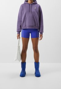 Fioletowa bluza z kapturem i kieszenią z przodu, niebieskie sportowe szorty z białym obszyciem, niebieskie ocieplane buty za kostkę oraz biały torba na ramię.