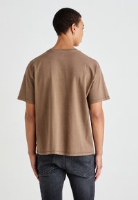 Rudas trumpomis rankovėmis marškinėliai, pagaminti iš minkštos medvilnės, su laisvu siluetu ir tiesiu kraštu. Minimalistinė dizaino koncepcija be matomų logotipų ar raštų.