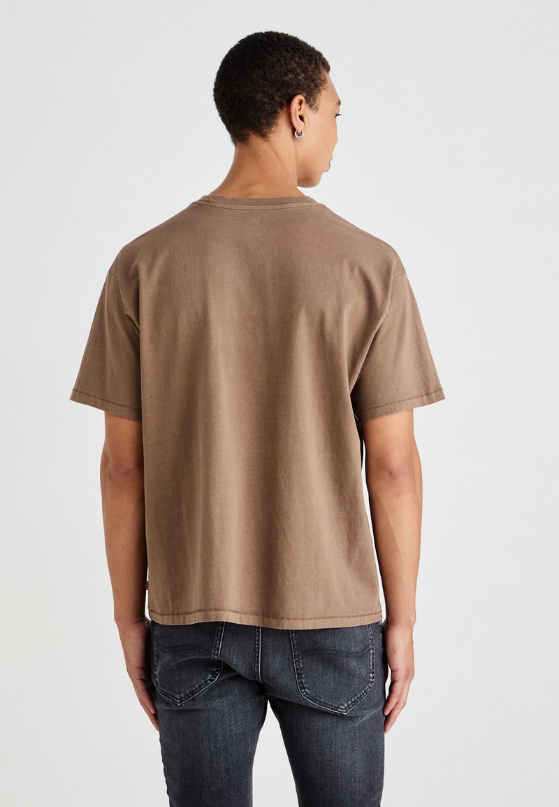 Braunes T-Shirt mit kurzen Ärmeln aus weicher Baumwolle, das einen lockeren Schnitt und einen geraden Saum hat. Minimalistisches Design ohne sichtbare Logos oder Muster.