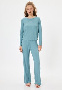 Conjunto de loungewear de color turquesa con textura acanalada que incluye una parte superior de manga larga con escote redondo y pantalones sueltos a juego con un dobladillo deshilachado.