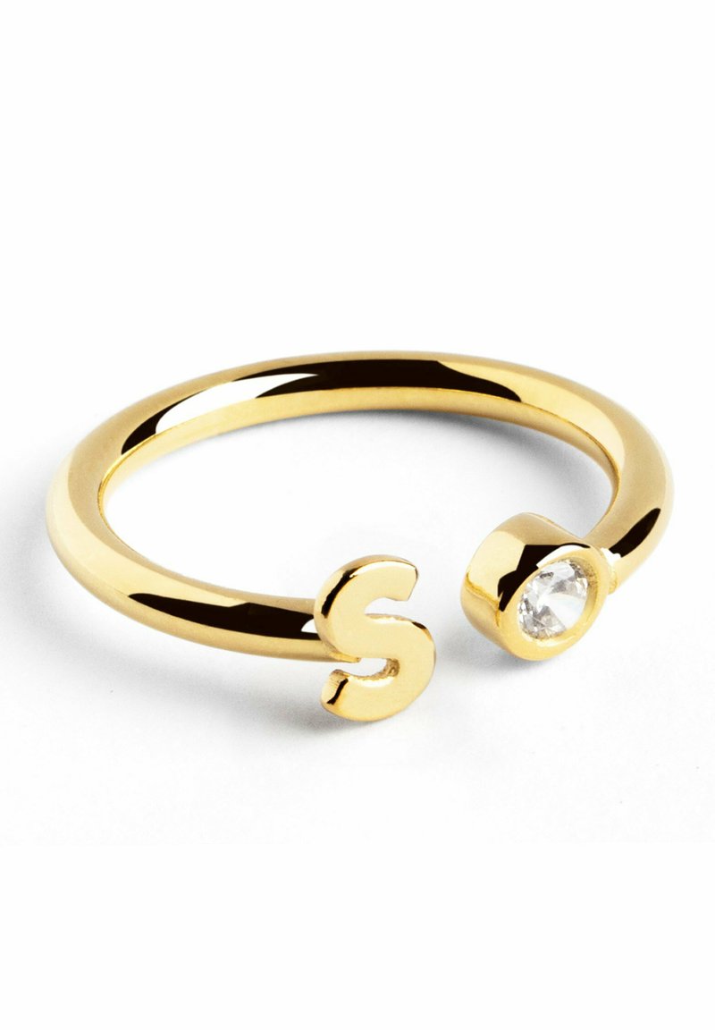 Anello in tono dorato con design aperto, caratterizzato da una "S" stilizzata su un'estremità e da una pietra circolare trasparente sull'altra. Superficie liscia e lucidata.