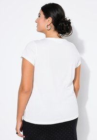 Witte t-shirt met korte mouwen, gemaakt van een zachte stof en met een ronde halslijn, gecombineerd met een zwarte rok met stippen. Gezicht vanuit de achterkant.
