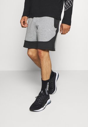 Szaro-czarne sportowe szorty z bocznymi kieszeniami, zestawione z czarnymi trampkami i wzorzystymi skarpetkami. Szorty mają teksturowane wykończenie.