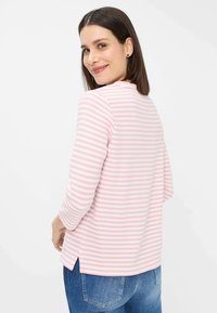 Leichtes Langarmoberteil in pink-weißen Streifen, gerippte Textur, runder Ausschnitt, seitliche Schlitz, kombiniert mit blauen Jeans.