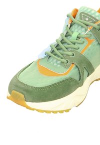 Grüne Sneakers aus Mesh und Wildleder, mit orangefarbenen Akzenten, strukturierten Stoffbereichen und einer dicken, weißen Gummi-Zwischensohle.