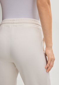 Light beige sweatpants made of soft fabric, featuring an elastic waistband and side pockets. Smooth texture with a straight leg design.