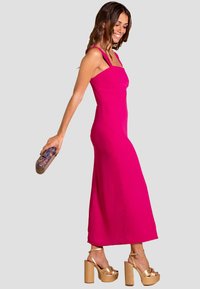 Vestido sin mangas fucsia con escote cuadrado y silueta ajustada, combinado con sandalias de plataforma doradas y sosteniendo un clutch brillante.