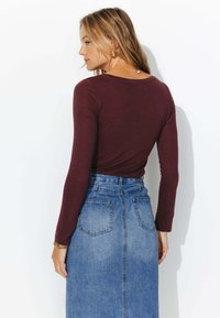 Haut à manches longues bordeaux associé à une jupe en denim taille haute. La jupe a un design structuré et deux poches à l'arrière.