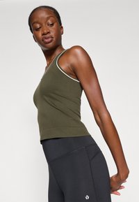 Ελαιόλαδο πράσινο στενό τοπ με λευκό περίγραμμα, ριγωτή υφή και σχέδιο V-λαιμού, συνδυασμένο με μαύρα ψηλόμεσα κολάν με λεπτομέρειες στα ράμματα.