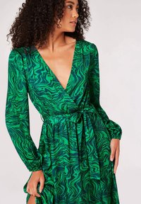 Robe verte avec un motif ondulé dans des nuances variées de vert, manches longues, décolleté en V plongeant et détail de taille nouée. Texture du tissu lisse.