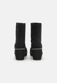 Bottines noires avec tige en tricot côtelé et talon bloc épais. Présente un accent gris le long de la semelle. Texture lisse avec un design ajusté.