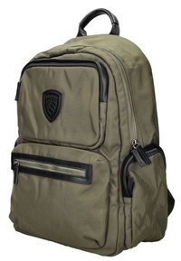 Sac à dos en nylon vert olive avec des accents en cuir noir, plusieurs compartiments zippés, tissu texturé et un logo en forme de bouclier bien en vue.