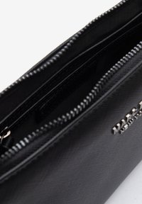 Zwarte gestructureerde leren tas met een ritssluiting, voorzien van een binnenzak en zilverkleurige hardware met logo-details. Glad gevoerd interieur.