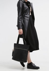 Sac fourre-tout en cuir noir avec fermeture éclair sur le dessus, ornée d'un pompon et de détails métalliques. Texture lisse, forme rectangulaire avec des anses robustes.