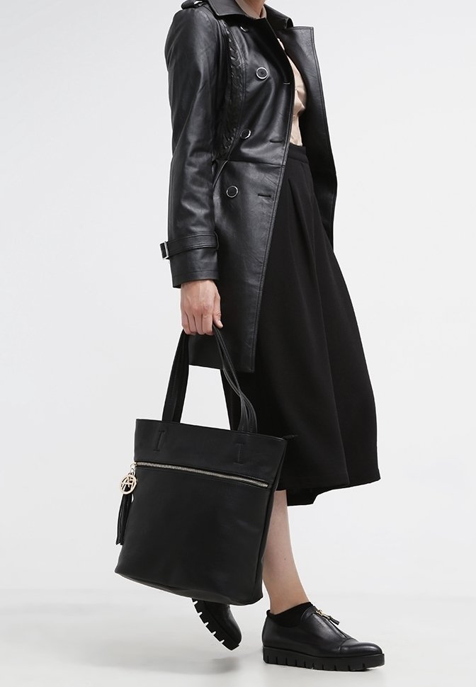 Sac fourre-tout en cuir noir avec fermeture éclair sur le dessus, ornée d'un pompon et de détails métalliques. Texture lisse, forme rectangulaire avec des anses robustes.