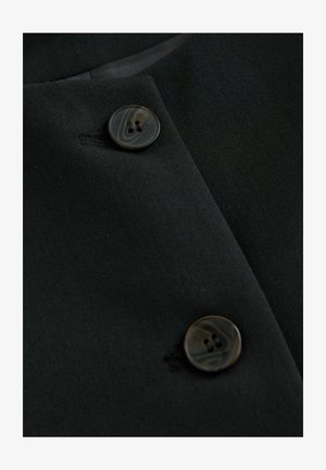 Fekete szövet közeli kép két kerek, mintás gombbal és texturált felülettel, alatta enyhe csillogással a mögöttes anyagból.