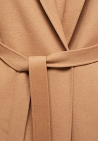Gros plan d'un manteau en laine beige avec de larges revers et une ceinture assortie nouée à la taille.
