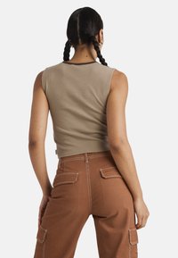 Szary prążkowany crop top z kontrastującymi brązowymi wykończeniami, w połączeniu z rudymi spodniami cargo z kieszeniami i widocznymi detalami szwów.