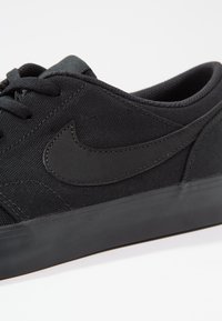 Baskets en toile noires avec une surface texturée, bout arrondi, lacets noirs et un logo noir mat sur le côté ; semelle en caoutchouc pour plus de durabilité.