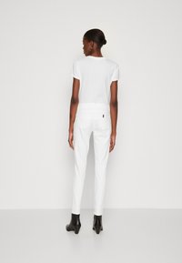 T-shirt bianco in cotone e pantaloni bianchi aderenti, con tasche posteriori. Modella che indossa stivaletti neri con tacco, vista di spalle.