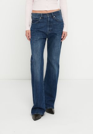 Blue denim flared jeans with a high waist, five-pocket design, light fading, and subtle stitching details, worn with pointed black shoes.