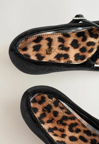Pantofi negri fără șireturi cu un exterior din țesătură texturată. Interiorul prezintă un model cu imprimeu leopard pe un fundal aurit metalizat.