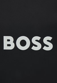 Un fundal texturat negru prezintă cuvântul "BOSS" în litere albe îngroșate și ridicate, cu un model de diamant.