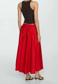 Jupe maxi rouge avec une taille froncée et un tissu fluide. Associée à un débardeur sombre ajusté et des sandales à talons noires.