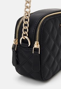 Borsa a tracolla nera trapuntata con hardware in tonalità oro, doppi zip e una tracolla a catena. Presenta una texture in pelle liscia e una forma rettangolare.