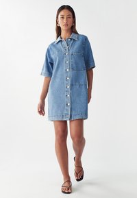 Denim hemdjurk in lichtblauw. Heeft korte mouwen, een knoopsluiting aan de voorkant en een borstzak. Zachte textuur en rechte snit.
