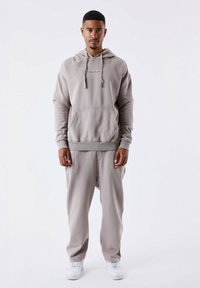 Felpa grigia in cotone con tasca frontale e cordini, abbinata a pantaloni della tuta coordinati. Sneakers bianche completano l'outfit rilassato.
