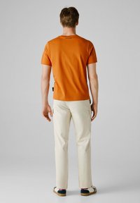 Orange bomulds T-shirt med rund hals, udstyret med et logo på ryggen. Kombineret med cremede cargo bukser, der viser lommer og en lige pasform.