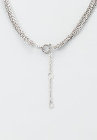 Silver flertrådig halsband med ett runt spänne och en justerbar kedjeförlängning. Har en glänsande, slät metallfinish.