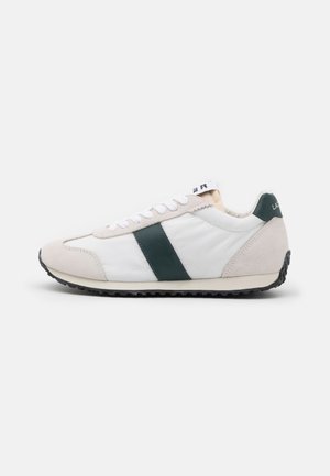 Baskets dotées d'une tige en cuir blanc avec des accents en suède vert, un bout en suède gris, des lacets plats blancs et une semelle en caoutchouc noire texturée.