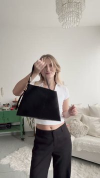 Μαύρη τσάντα χειρός με τριγωνικό σχήμα, από μαλακό σουέντ υλικό και κοντό λουράκι. Μινιμαλιστικός σχεδιασμός χωρίς εμφανή μεταλλικά μέρη ή σχέδια.