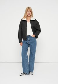 Μαύρο δερμάτινο μπουφάν με ψεύτικη γούνα στο γιακά, συνδυασμένο με άσπρη πλεκτή μπλούζα και μπλε τζιν ψηλόμεσα. Μαύρα αθλητικά ολοκληρώνουν το σύνολο.