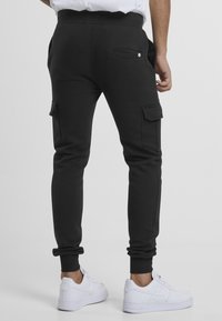 Black cargo sweatpants with a tapered fit, elastic waistband, side pockets, and cuffed hems. Paired with white sneakers.