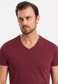Burgundské tričko s výstřihem do V vyrobené z hladké bavlněné tkaniny, s krátkými rukávy a přiléhavým střihem. Minimalistický styl bez vzorů nebo akcentů.