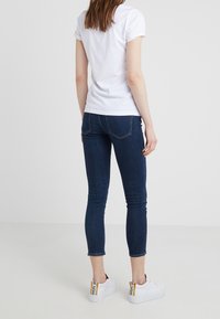 Camiseta blanca de algodón con mangas enrolladas, combinada con jeans ajustados azul oscuro. Zapatillas blancas con detalles de acento en el talón.
