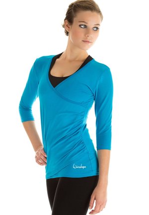 Turquoise athletic top with three-quarter sleeves, v-neck design, and gathered side detailing. Made from stretch fabric for mobility.