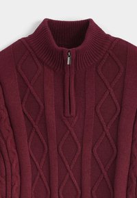 Pull-over bordeaux avec col montant côtelé, présentant des motifs losanges et torsadés, ainsi qu'une fermeture éclair frontale avec tirette métallique.
