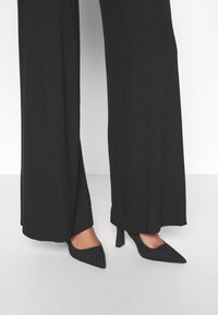 Czarne szerokie spodnie połączone z czarnymi szpilkami o spiczastym nosku, charakteryzujące się eleganckim krojem i teksturowanym materiałem dla gładkiego wykończenia.