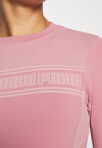 Růžové atletické tričko s dlouhým rukávem, vyrobené z texturované látky s puntíkovaným vzorem a jemným logem PUMA na prsou. Hladké švy a přiléhavý střih.