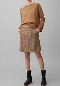 Brun strikket sweater med løs pasform, beige ternet nederdel med blå og brune striber, og sorte ankelstøvler. Nederdelen har sidelommer.