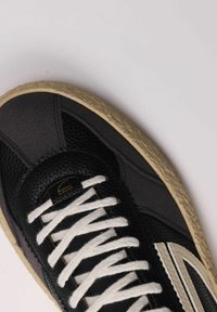 Sneaker nera con tomaia in pelle testurizzata, lacci bianchi e suola in gomma beige con un aspetto leggermente consumato.