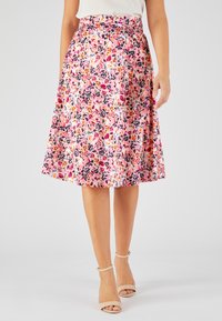 Falda midi floral con fondo rosa y flores multicolores, diseño plisado y cinturón en la cintura. Combinada con sandalias de tira al tobillo beige.