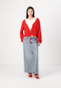 Cardigã vermelho tricotado com fecho de laço, top justo branco, saia maxi de ganga azul e sapatos de salto alto vermelhos com detalhes em prata.