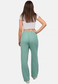 Licht teal, wijde broek gemaakt van textuurmateriaal, met een elastische tailleband en een relaxte pasvorm. Witte cropped top zichtbaar boven de tailleband.